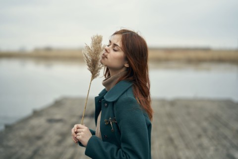 Caucasian woman standing on dock smelling stalk of grass