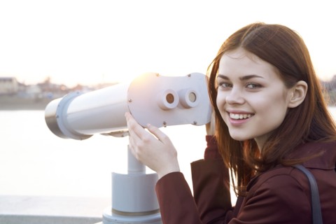 Smiling Caucasian woman using binoculars at waterfront