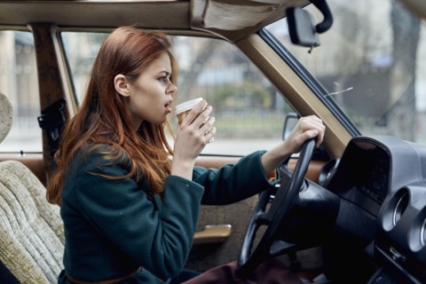 Angry Caucasian woman driving car and drinking coffee