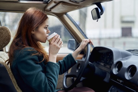 Caucasian woman driving car and drinking coffee