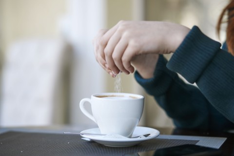 Caucasian woman pouring sugar into coffee
