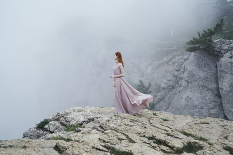 Caucasian woman wearing dress on rock in fog