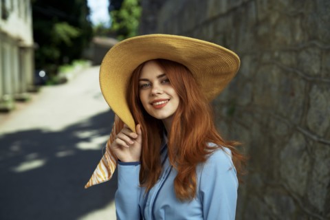 Smiling Caucasian woman wearing hat near stone wall