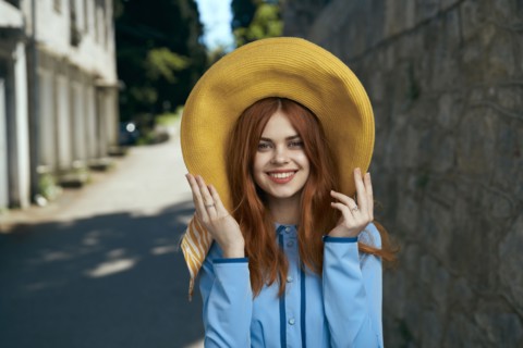 Smiling Caucasian woman wearing hat near stone wall