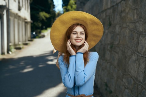 Smiling Caucasian woman wearing hat near stone wall