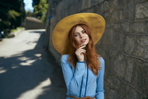 Smiling Caucasian woman wearing hat near stone wall