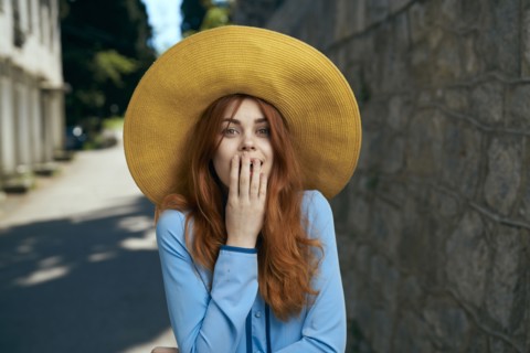 Surprised Caucasian woman wearing hat near stone wall
