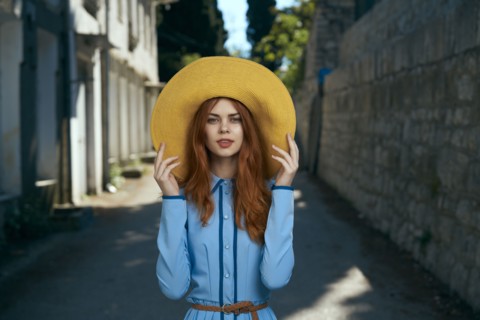 Smiling Caucasian woman wearing hat near stone wall