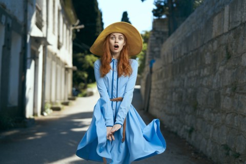 Surprised Caucasian woman wearing hat near stone wall