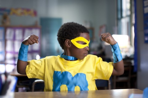African American boy wearing superhero costume in classroom