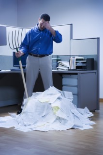 Businessman overlooking mountain of paper and holding rake