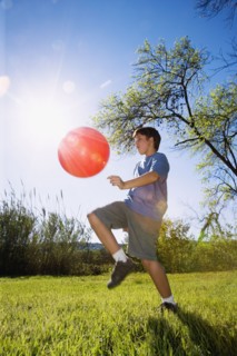 Boy kicking ball in bright sunlight