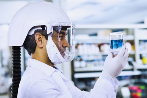 Indian male scientist wearing respirator and looking at beaker