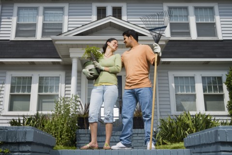 Hispanic couple with gardening tools in front of house