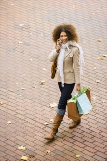 Hispanic woman walking with cell phone and shopping bags