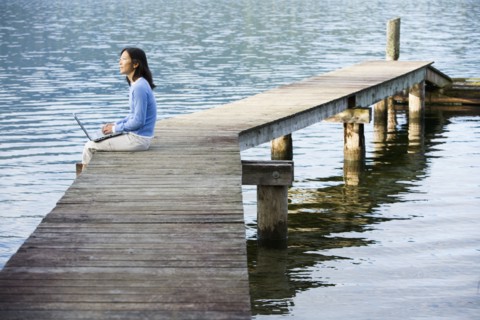 Asian woman holding laptop on edge of pier