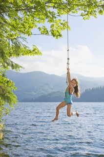Asian girl hanging from lake rope swing