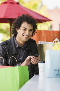 Middle Eastern man with shopping bags text messaging on cell phone