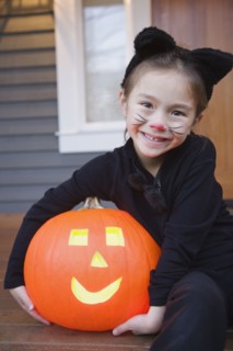 Mixed race young girl in cat costume holding Halloween pumpkin