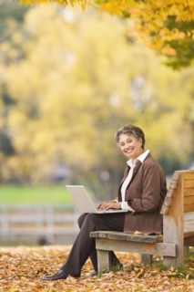 African woman using laptop on park bench in autumn