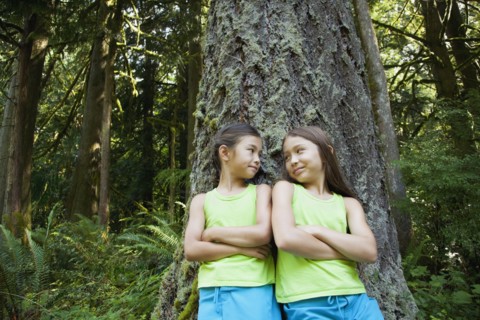 Mixed race girls leaning on tree