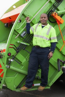 Black man riding on back of garbage truck
