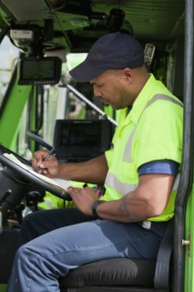 African American man in garbage truck writing on clipboard