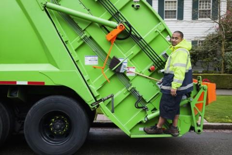 Pacific Islander man riding on garbage truck