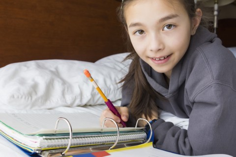 Mixed race girl doing homework on bed