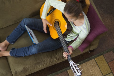 Mixed race girl practicing guitar on sofa