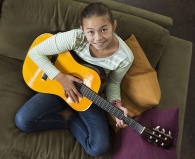 Mixed race girl practicing guitar on sofa