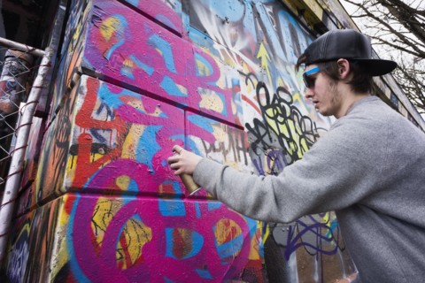 Caucasian boy spraying graffiti on urban wall