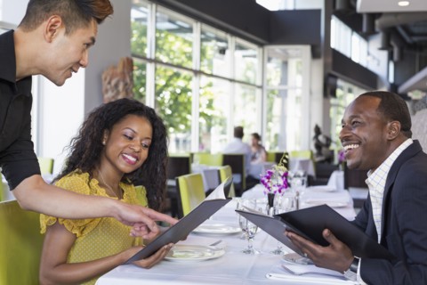 Waiter explaining menu to couple in restaurant