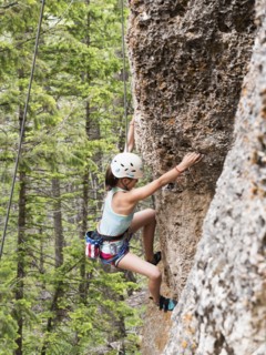 Mixed race girl climbing steep cliff