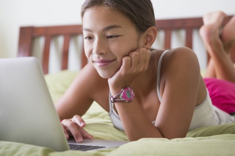 Mixed race girl using laptop on bed