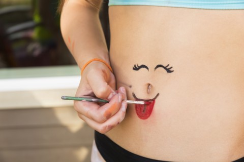 Mixed race girl painting face on stomach
