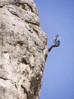 Caucasian man climbing rock gesturing with tongue out