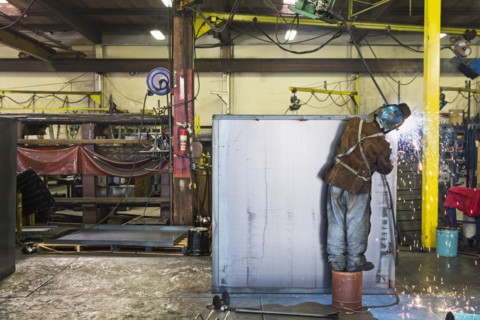 Asian worker grinding metal container in factory