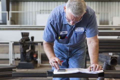 Caucasian worker using calculator in factory
