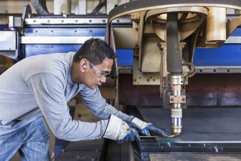 Asian worker fabricating metal in factory