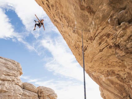 Mixed Race girl hanging from rope while rock climbing