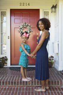 Smiling mixed race mother and daughter standing on front stoop