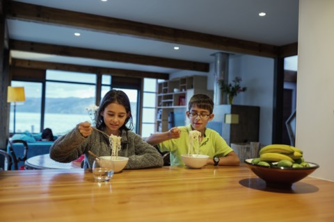 Mixed race children eating noodles at table
