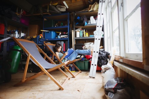 Mixed race girl reading in lawn chair in shed