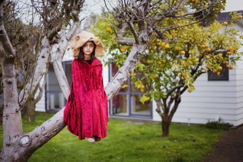 Mixed race girl in witch costume sitting in tree