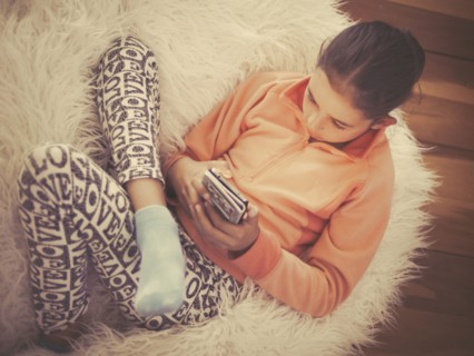 Mixed race girl using cell phone on in furry chair
