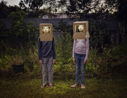 Mixed race children wearing cardboard astronaut helmets in backyard