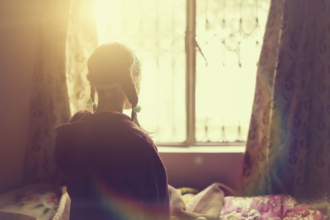 Mixed race girl looking out bedroom window