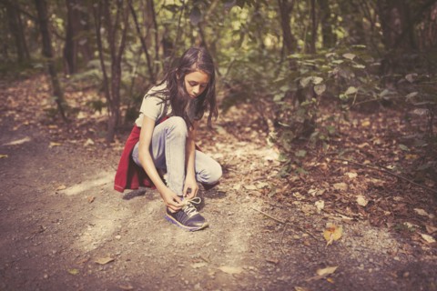 Mixed race girl tying shoelaces on dirt path