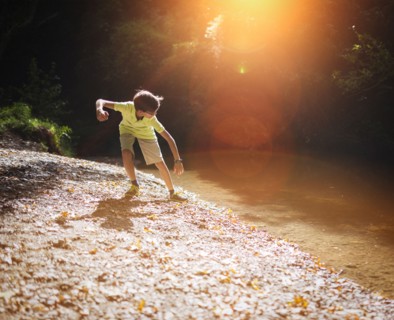 Mixed race boy skipping stones in stream